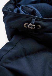 Jachetă puffer albastră marină dintr-un material cu o textură netedă, având o glugă cu șnur, accesorii metalice și un design matlasat.
