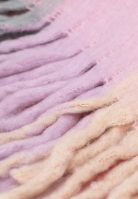 Długi wełniany szal w pastelowych różowych i kremowych kolorach, o miękkiej teksturze i frędzlach na krawędziach tworzących efekt warstw.