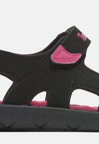 Mustat sandaalit, joissa on vaaleanpunaisia yksityiskohtia, tekstuurilla varustettu hihna, kuusikulmainen kuvio sekä mukautuva pohja mukavuutta varten.