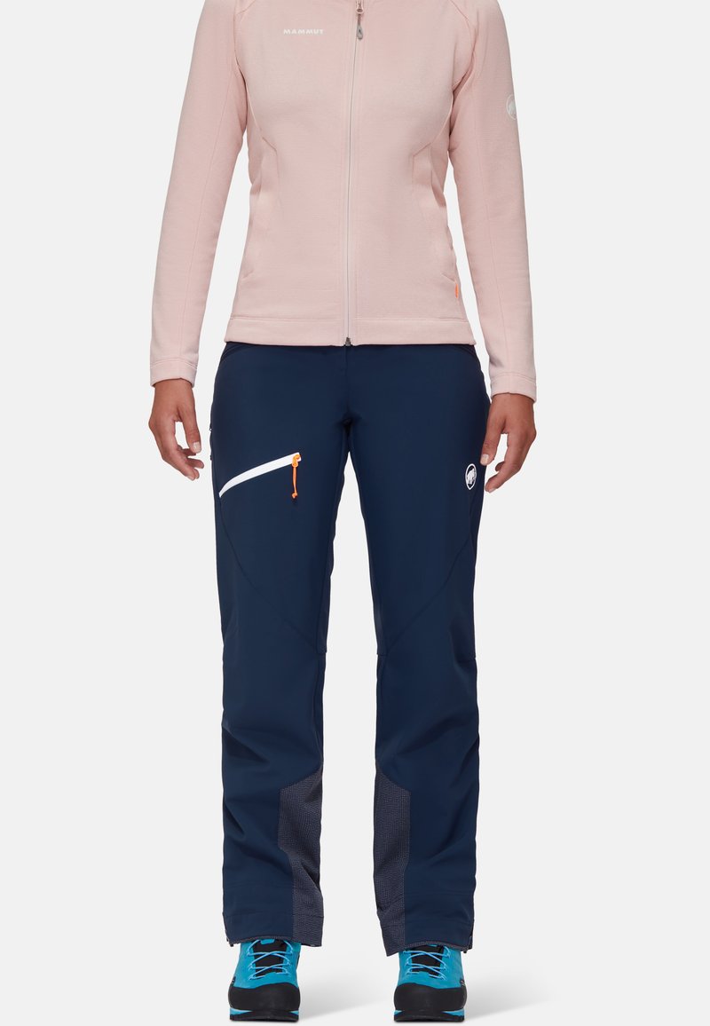 Kurtka polarowa w jasnoróżowym kolorze, z pełnym zamkiem, z długimi rękawami. Ciemnoniebieskie spodnie narciarskie z białymi akcentami zamka i szarymi siateczkowymi detalami przy kostkach.