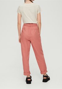 Camiseta de manga corta de color beige claro, combinada con pantalones rosa de tiro alto y con dobladillo enrollado, y zapatos negros tipo slip-on.