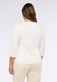 Haut clair à manches longues avec des manches trois-quarts et une broderie décorative aux poignets, associé à un pantalon beige.