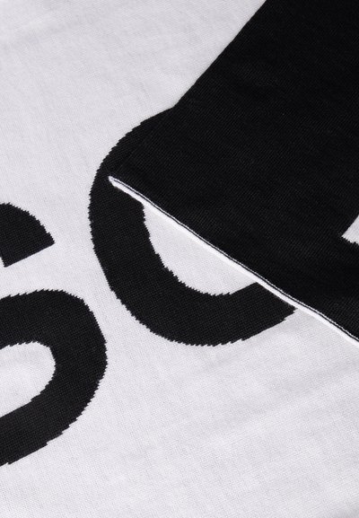 Gros plan sur un tissu noir et blanc avec de grandes lettres noires partiellement visibles sur un fond blanc, et un bord de tissu noir qui se chevauche.