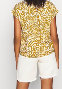 Top corto giallo e bianco a maniche corte con una stampa animale a spirale, abbinato a pantaloni corti con orlo sfrangiato di colore bianco sporco.
