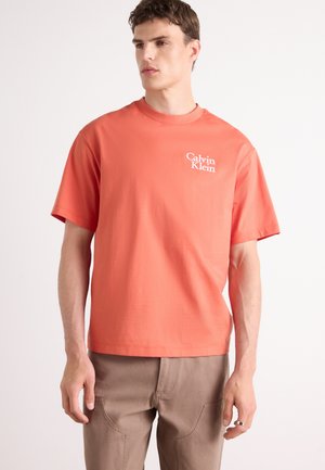 Koraalkleurig t-shirt met korte mouwen van katoen, met een klein wit logo op de linkerborst. Ontspannen pasvorm met een ronde hals.