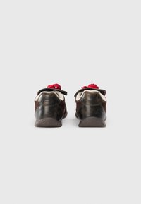 Brown leather shoes with a textured finish, contrasting red laces, soft inner lining, and a rubber sole with a zigzag pattern.