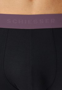 Crne bokserice sa tamno ljubičastim elastičnim pojasom na kojem je suptilni uzorak s natpisom "SCHIESSER". Glatka tkanina i prilagođeni kroj.