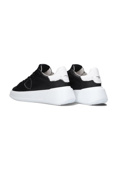 Black leather sneakers with white accents, featuring a chunky white sole, rounded shape, and minimalistic design. Rubber outsole with textured grip.