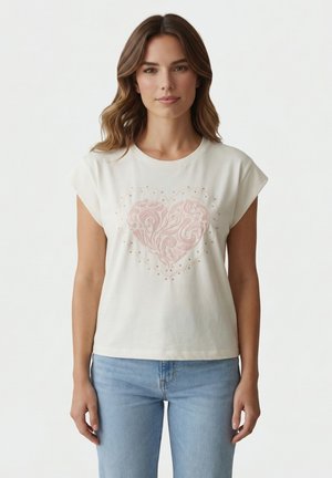 Donna che indossa un top bianco senza maniche con un design a cuore rosa testurizzato, abbinato a jeans azzurri, in piedi contro uno sfondo semplice.