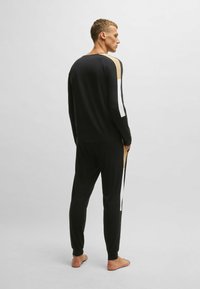 Ensemble de détente noir comprenant un haut à manches longues et un pantalon avec des blocs de couleur beige et blanc. Tissu doux et design ajusté.