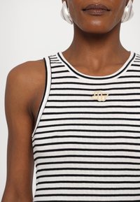 Haut sans manches à rayures noires et blanches avec une texture côtelée ; présente un accent doré au centre. Encolure ronde, design ajusté.