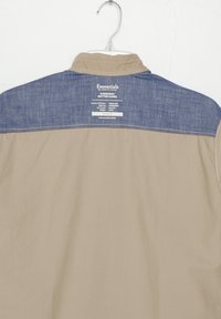 Camisa de mezclilla de botones de corduroy con cuerpo beige y canesú azul denim. Presenta detalles de etiqueta en la parte posterior, tamaño mediano.