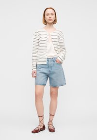 Λευκό ριγέ ζακέτα με στρογγυλή λαιμόκοψη, συνδυασμένη με ανοιχτό μπλε τζιν σορτς. Καφέ σανδάλια με λουράκια ολοκληρώνουν την εμφάνιση. Καθαρός, μίνιμαλ σχεδιασμός.