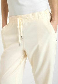 Lichtgele sweatpants gemaakt van zacht materiaal, met een elastische tailleband en koord. Inclusief zijzakken en subtiele zwarte accenten.