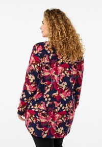 Tunic a maniche lunghe di colore blu navy con un motivo floreale multicolore che presenta tonalità di rosa, beige e marrone; tessuto morbido con una vestibilità rilassata.