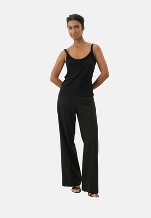 Black tank top with wide straps paired with loose-fitting black trousers; smooth fabric, straight cut, minimal accents, and sandals.