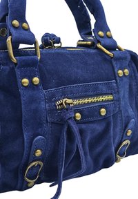 Sac à main en suède bleu marine avec quincaillerie dorée, doté d'une poche frontale zippée et de rivets décoratifs. Les courtes poignées sont fixées par des attaches en métal.