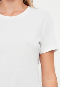 Biała koszulka z okrągłym dekoltem i krótkimi rękawami, wykonana z miękkiego, lekkiego materiału. Posiada prosty design bez widocznych logo ani wzorów.