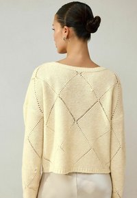 Cremefarbener Strickpullover mit boxy Design, featuring Rautenmuster und offenen Details. Verkürzter Saum und weiter Ausschnitt.