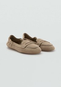 Mocasines de ante beige con una textura suave, diseño de slip-on y detalle de costura decorativa en la parte superior. Suela de goma flexible.