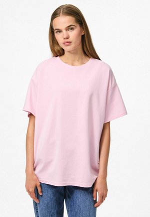 T-shirt di cotone rosa chiaro con maniche corte e vestibilità rilassata, caratterizzata da un collo rotondo e una texture liscia. Abbinato a jeans in denim blu.