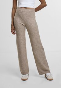 Béžové kalhoty s širokými nohavicemi vyrobené z měkkého, strukturovaného pleteného materiálu. Mají vysoký elastický pas a žebrované detaily na kotnících.