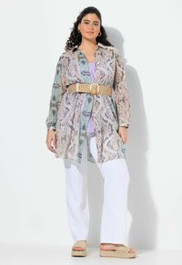 Camicia button-up multicolore in tessuto traslucido, con un motivo astratto, strizzata con una cintura intrecciata dorata, abbinata a pantaloni bianchi a gamba larga.