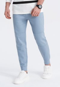 Lichtblauwe joggingsbroek gemaakt van zachte stof, met strakke boorden en paneel details. Gecombineerd met witte sneakers voor een casual look.