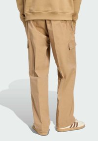 Pantalones cargo en color caqui con ajuste relajado, que cuentan con dos bolsillos laterales y una textura acanalada. Combinados con zapatillas deportivas en color crema con franjas marrones.