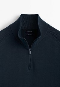 Dunkelblaues Viertel-Reißverschluss-Pullover mit geripptem hohen Kragen und Schulterdetails, teilweise geöffneter Reißverschluss, flach auf einem weißen Hintergrund ausgelegt.