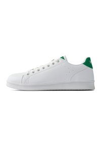 Zapatilla blanca con parte superior de cuero sintético suave, acento verde en el talón, cierre de cordones y suela de goma plana, con perforaciones para mejorar la transpirabilidad.