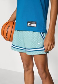 Nike basketball shorts in mint green with a checkered pattern, side stripes, and a white logo. Pairing blue athletic top and orange basketball.