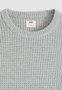 Grå strikkegenser med ribbet tekstur, rund halsutskjæring, og merket som standard passform. Merket inkluderer merkevaren "Levi's" og størrelse "M."