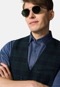 Ciemnozielona kamizelka w kratkę na jasnoniebieskiej koszuli w wzory, z kieszenią na piersi i stójką. Dopełnieniem wyglądu są czarne okrągłe okulary przeciwsłoneczne.