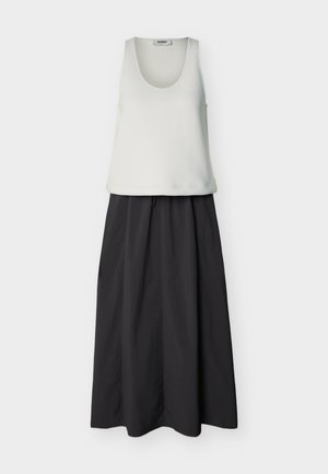 Balta bezroku tvertnes topiņa ar dziļu apaļu kakla izgriezumu kopā ar augsta vidukļa, garu melnu svārku ar viegliem plisējumiem.