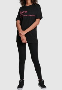 Camiseta negra de algodón con mangas cortas, con texto rosa "amor" y definición, combinada con mallas negras y zapatillas altas.