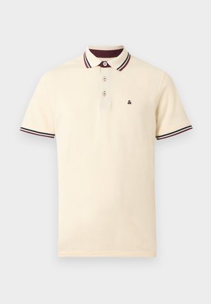 Kreemikas lühikeste varrukatega polosärk, millel on kolm nööpi, burgundia ja musta triibulise krae ning varrukate servad ning väike burgundia värvi &-logo rinnal.