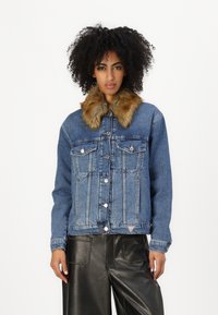 Denim jacket with a faux fur collar, blue color, button closure, two chest pockets, and a triangular logo on the hem. Textured fabric.