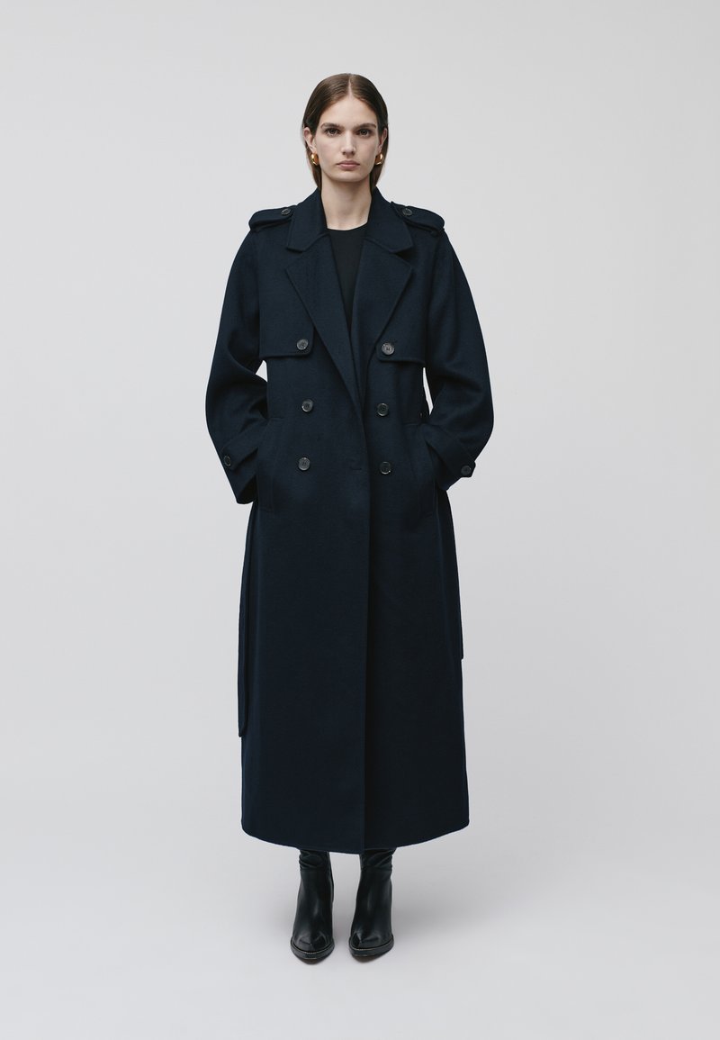 Granatowy wełniany płaszcz trench z podwójnym zapięciem na guziki, epoletami na ramionach, dużymi kieszeniami i długą, prostą sylwetką.