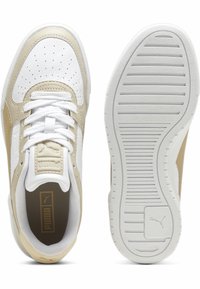 Beige és fehér sportcipők sima bőr felsőrésszel, perforált orr résszel, lapos fehér fűzőkkel és texturált gumitalppal, amely vízszintes barázdákkal rendelkezik.