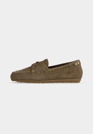Mocassin en daim marron avec des clous ronds dorés le long des bords et une semelle en caoutchouc plate sur un fond gris uni.
