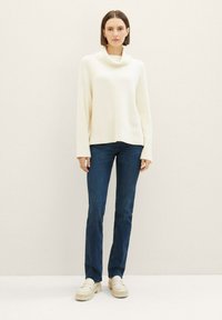 Kremfarget skjerf genser med ribbestruktur, kombinert med mørkeblå rette jeans og lysebeige platåloafers.