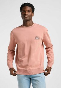 Jasnoróżowy sweatshirt z długimi rękawami, z prążkowanym dekoltem i dołem, z małym graficznym logo na lewej piersi i gładką fakturą.