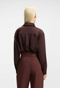 Blusa di seta color marsala con un fit rilassato, pieghe posteriori e maniche lunghe. Presenta un colletto classico e chiusura con bottoni ai polsini.