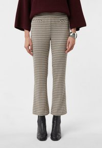 Spodnie w kratę w beżowo-brązowy wzór, charakteryzujące się eleganckim krojem, subtelnymi przednimi kieszeniami oraz szerszymi nogawkami, zestawione z czarnymi botkami do kostki.