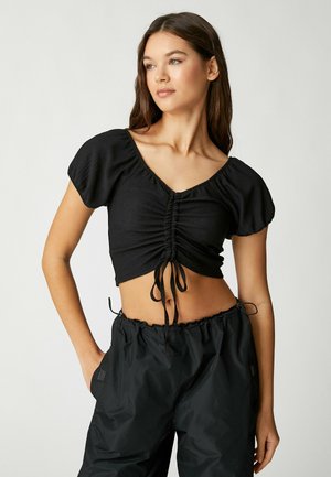 Czarny krótki top z krótkimi puff sleeves, marszczonym przodem i regulowanymi sznurkami. Połączony z czarnymi, luźnymi spodniami.