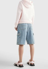 Světle růžová mikina s kapucí a stahovací šňůrkou, doplněná modrými denimovými šortkami s kapsami a švy. Černé a růžové sandály.