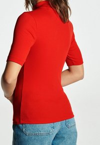 Rød ribbet polo t-shirt med korte ærmer og en mock neckline, der har en tætsiddende silhuet og slidser i siderne, parret med lys blå denim shorts.