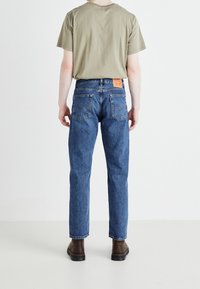 Mörkblå jeans med rak bendesign, med subtila broderidetaljer och två bakfickor. I kombination med en beige t-shirt och bruna stövlar.