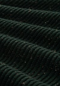 Donkere groene gebreide stof met een geribbelde textuur, voorzien van kleine spikkels in lichtere kleuren. Dikke en gezellige uitstraling.